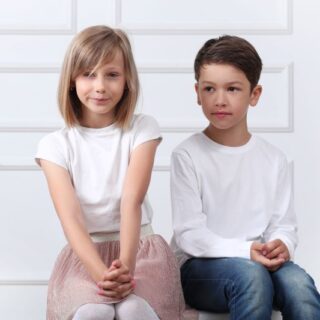 بنت ترتدي تنورة زهرية اللون وكنزة بيضاء تجلس بجانب صبي يرتدي كنزة بيضاء اللون وبنطال جينز